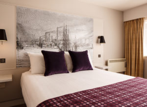 A double bed with picture headboard and purple cushions